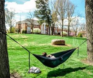 student in hammock in spring tied between trees, with Crounse library in background
